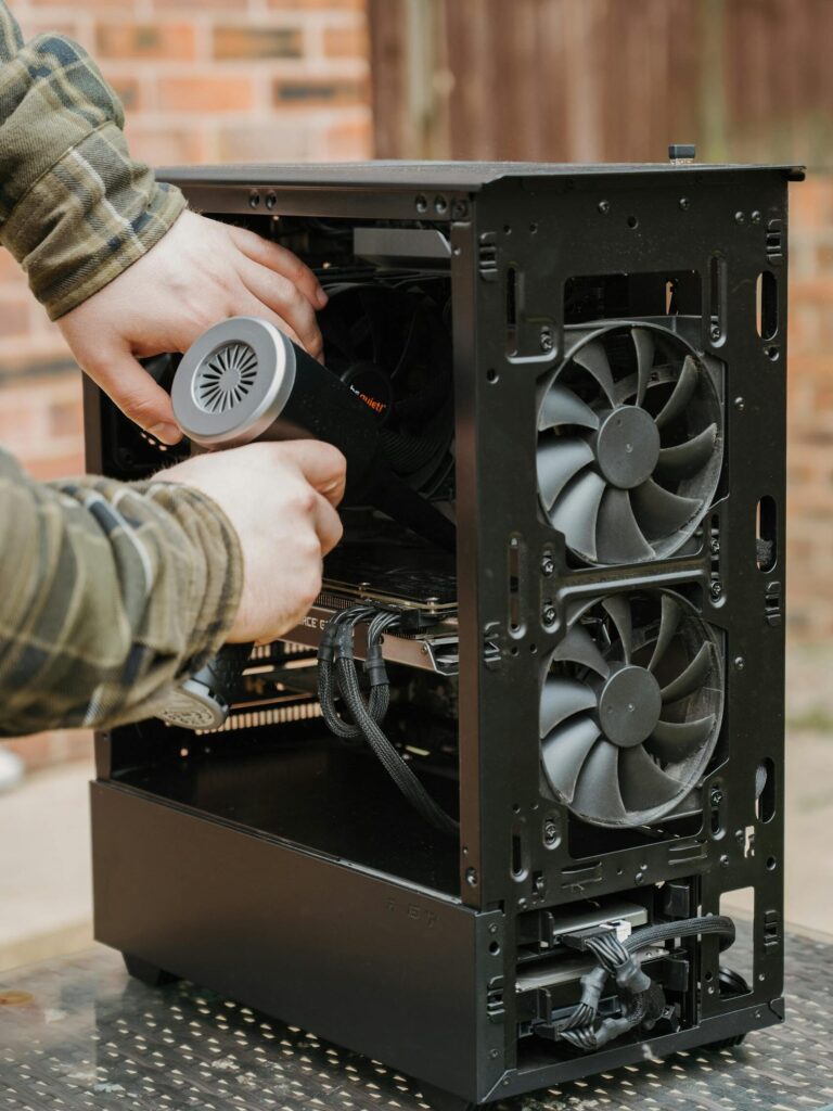 Hands cleaning a desktop PC case with an electric duster outdoors.